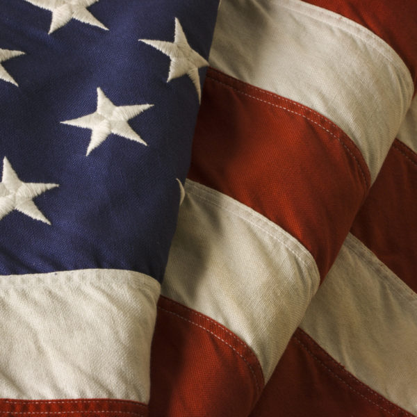 Old American flag of the United States of America, close-up. Also called Old Glory and Stars and Stripes, this banner is a patriotic decoration on Fourth of July (Independence Day), Memorial Day, Veterans Day, and other national holidays. With weathered thread embroidery stitching and faded red, white, and blue fabric.